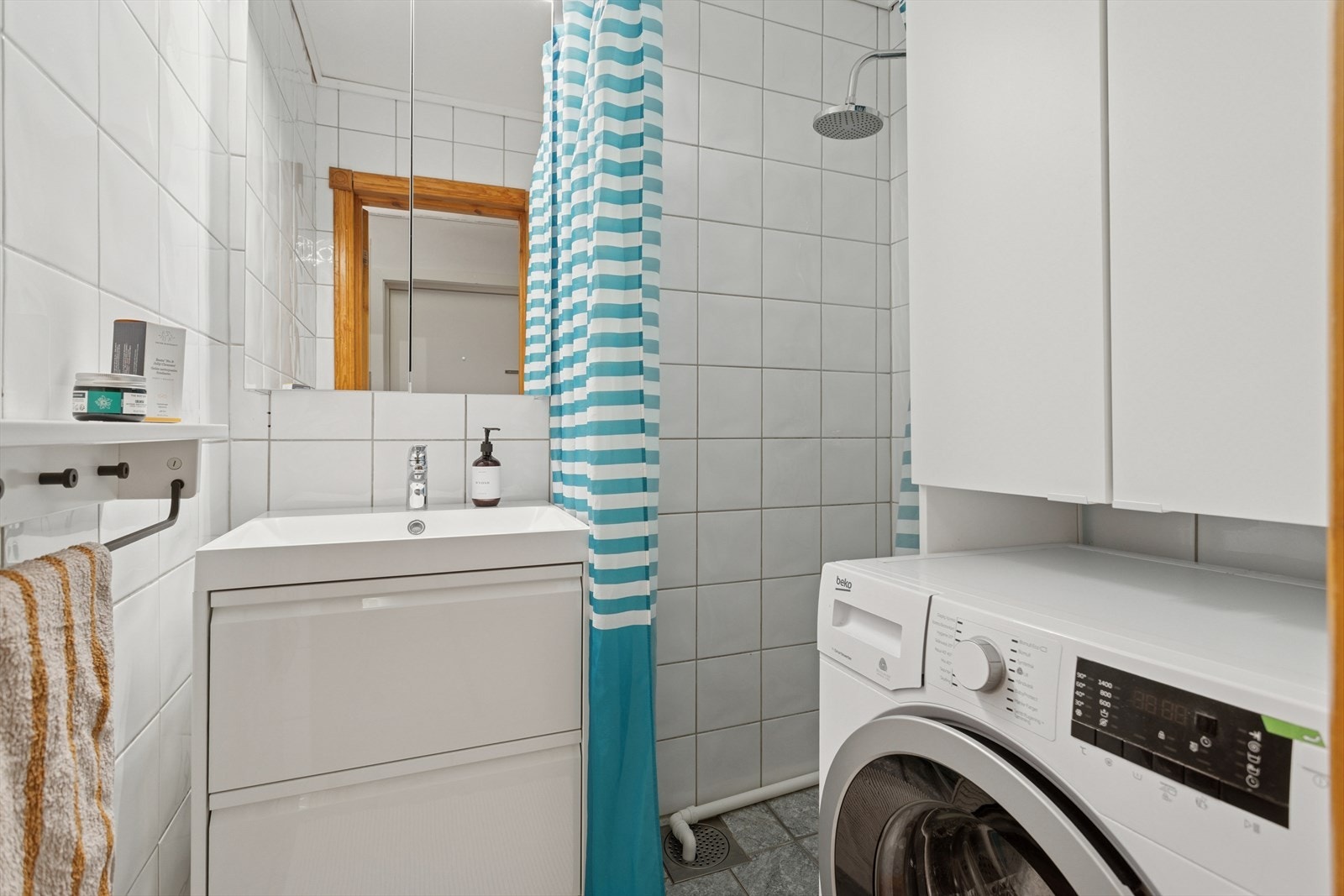 Baderommet er ca. 2,3 m² og har flis på gulv og vegg, og malt slett himling. Badet er utstyrt med en dusjnisje, innredning med servant og opplegg for vaskemaskin. Naturlig avtrekk. Vaskemaskin medfølger. Galleribilde