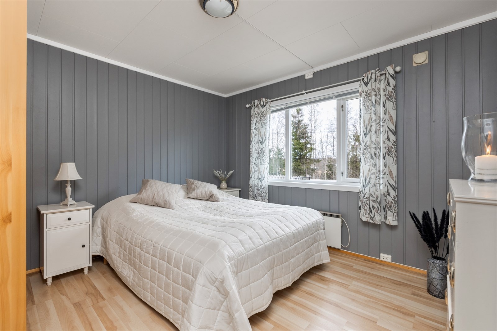 Lyst og fint soverom i 1. etasje med laminat på gulv, gråmalt panel på veggene og et stort vindu som slipper inn fint lys. På soverommet er det plass til dobbeltseng, kontorpult eller kommode, samt god oppbevaringsplass i garderobeskap. Galleribilde