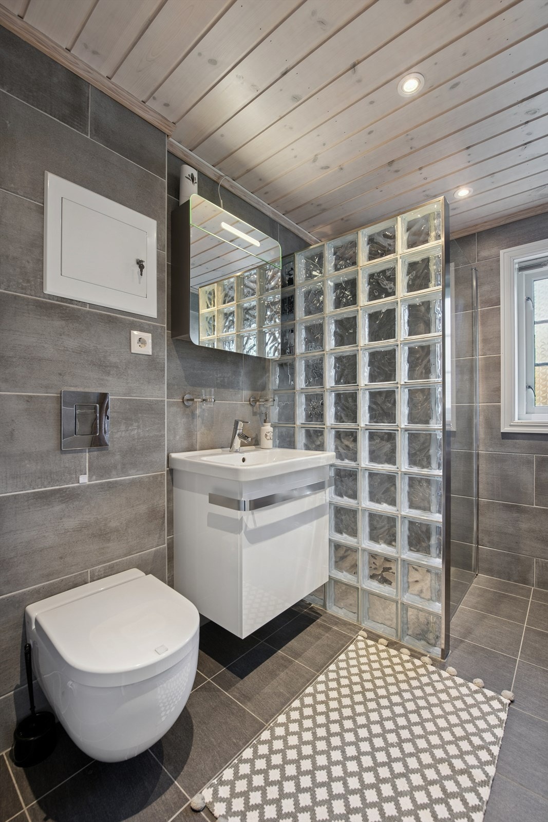 Pent helfliset bad med varmekabler i gulvet. Rommet inneholder servant med lys innredning, dusjnisje og veggmontert toalett. Galleribilde