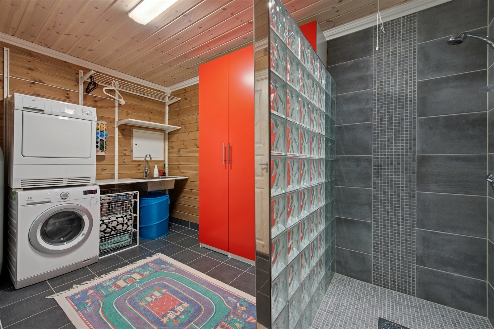 Funksjonelt vaskerom med fliser og varmekabler på gulvet, flislagte vegger og panel i himlingen. Her er det rikelig med oppbevaringsplass, og rommet egner seg godt til tørking av vått tøy og som kombinert garderobe. Galleribilde