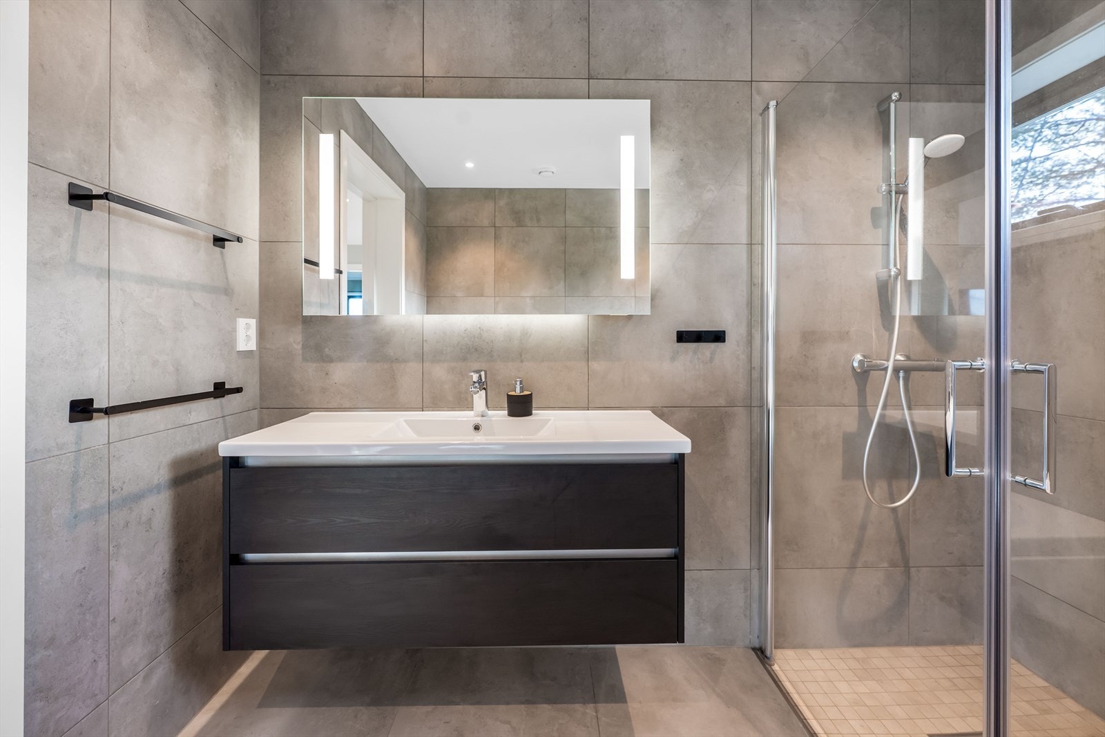 Moderne innredning med heldekkende servant, veggmontert toalett og innsvingbare glassdører. Galleribilde