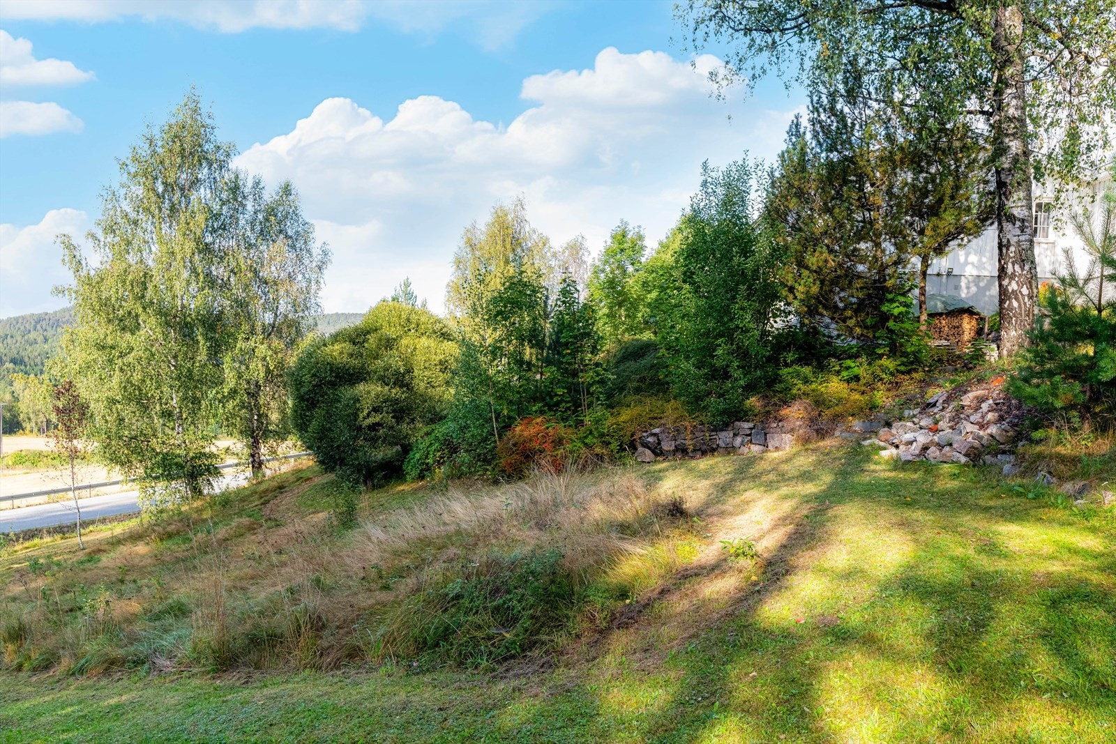 Skrånende tomt som ligger solrikt til. Tomten er opparbeidet med plen, trær og div prydbusker. Galleribilde