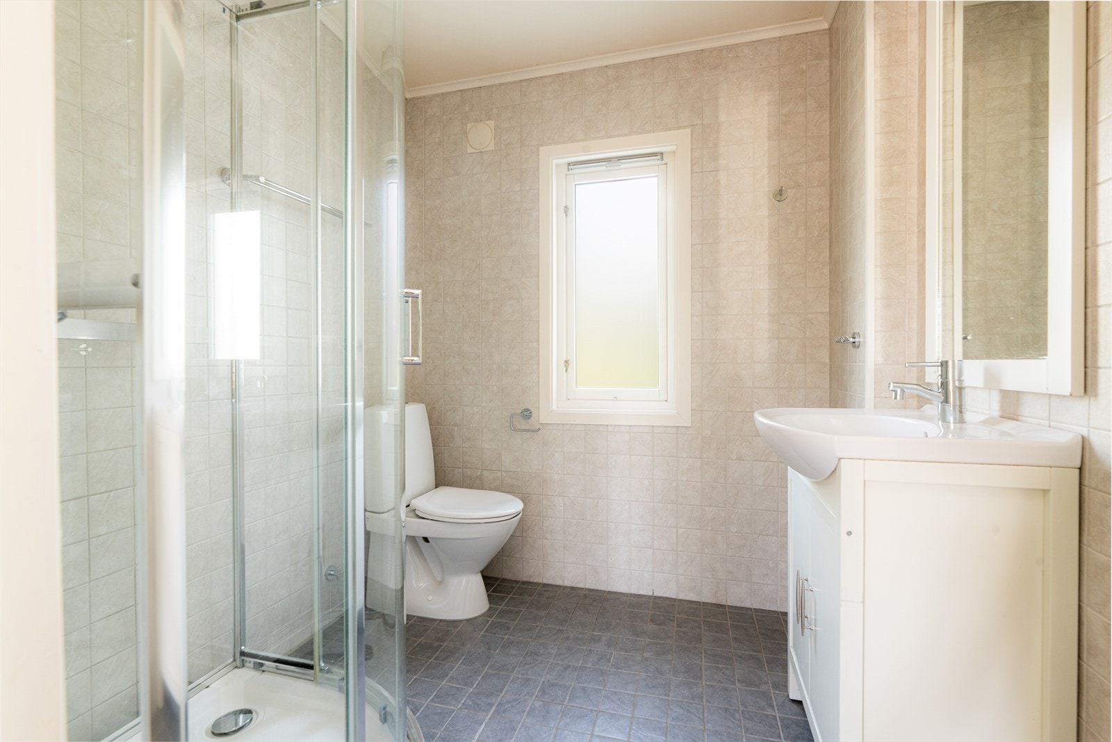 Bad i 1. etasje med overlater bestående av flis med varmekabler i gulv, flis på vegg og malt himling. Galleribilde