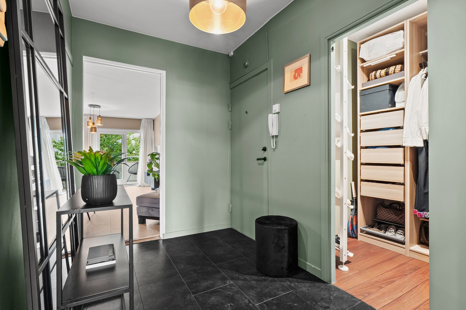 Vel inne har gangen flismønstret laminatgulv og dørcalling ved ytterdøren. Veggene, inkludert døren, er malt i en tidsriktig grønntone. Galleribilde