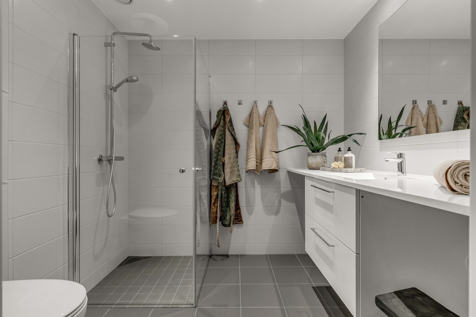 Badet i leiligheten er pent flislagt, og innredningen består av servant, speil, dusjhjørne, vegghengt toalett og opplegg for vaskemaskin. Galleribilde