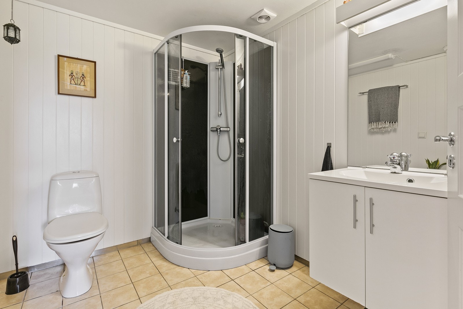 Badet har flislagt gulv med varmekabler, og er utstyrt med toalett, dusjkabinett og servant med skap og speil Galleribilde