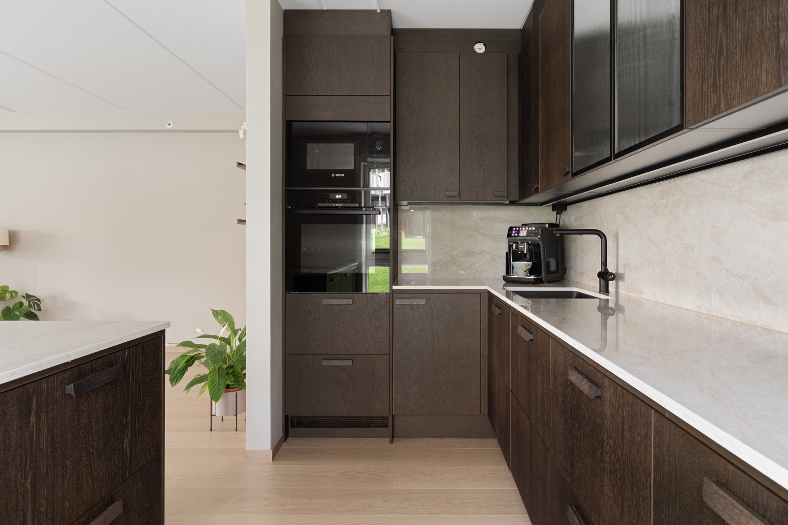 Her får du blant annet Dektonbenkeplate i stein, integrerte hvitevarer i arbeidshøyde, vinskap i kjøkkenøy, overskap med ornamentglassfronter og koketopp med nedfelt ventilator. Galleribilde