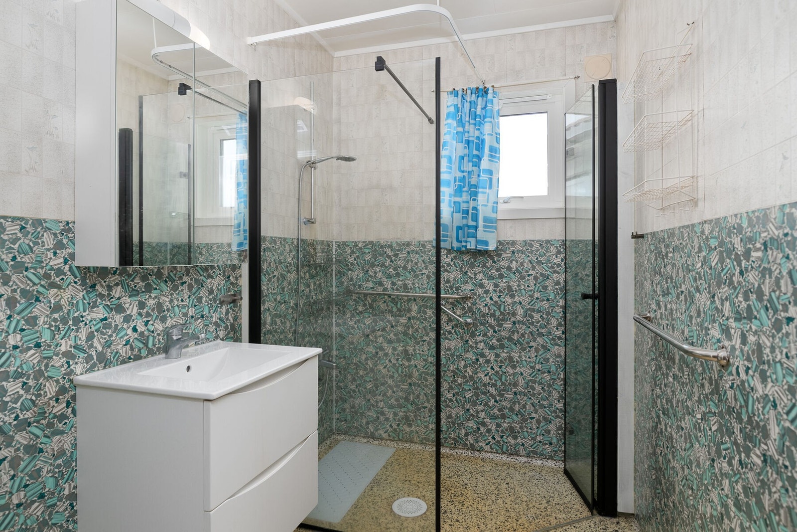 Eldre baderom med nyere innredning. Det er servant på skuffeseksjon, speilskap og dusjhjørne. Galleribilde