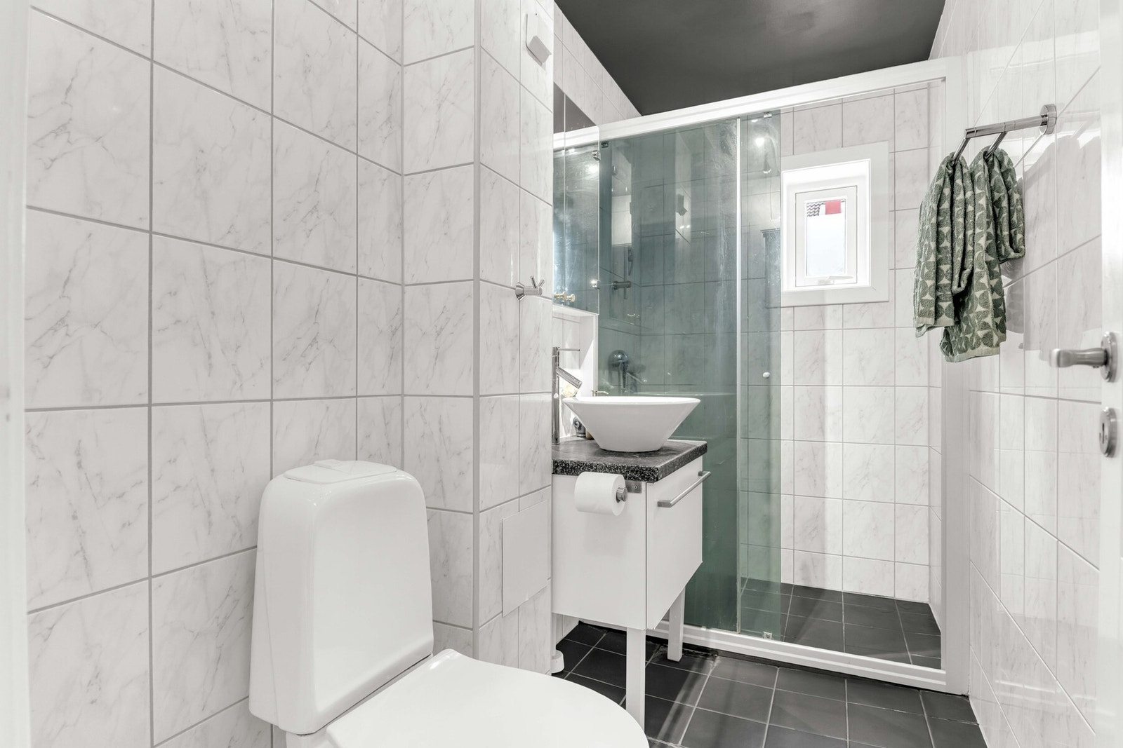 Varmekabler i gulvet sørger for en lun følelse hele året. Rommet er innredet med servant, speilskap med belysning, toalett og en dusjnisje med glassdører. Galleribilde