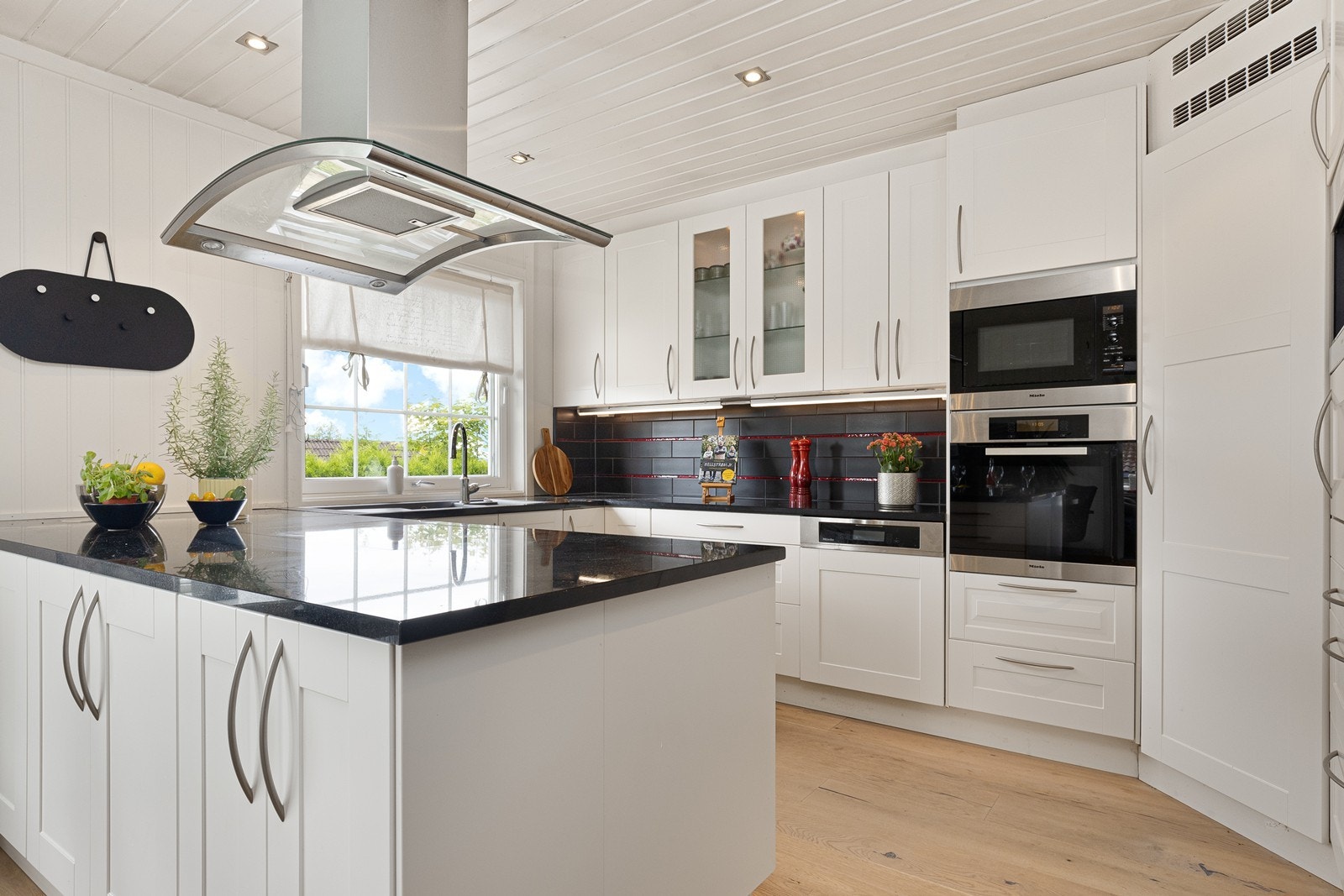 Velutstyrt kjøkken med steinbenkeplate, integrerte hvitevarer og kjølehjørne Galleribilde