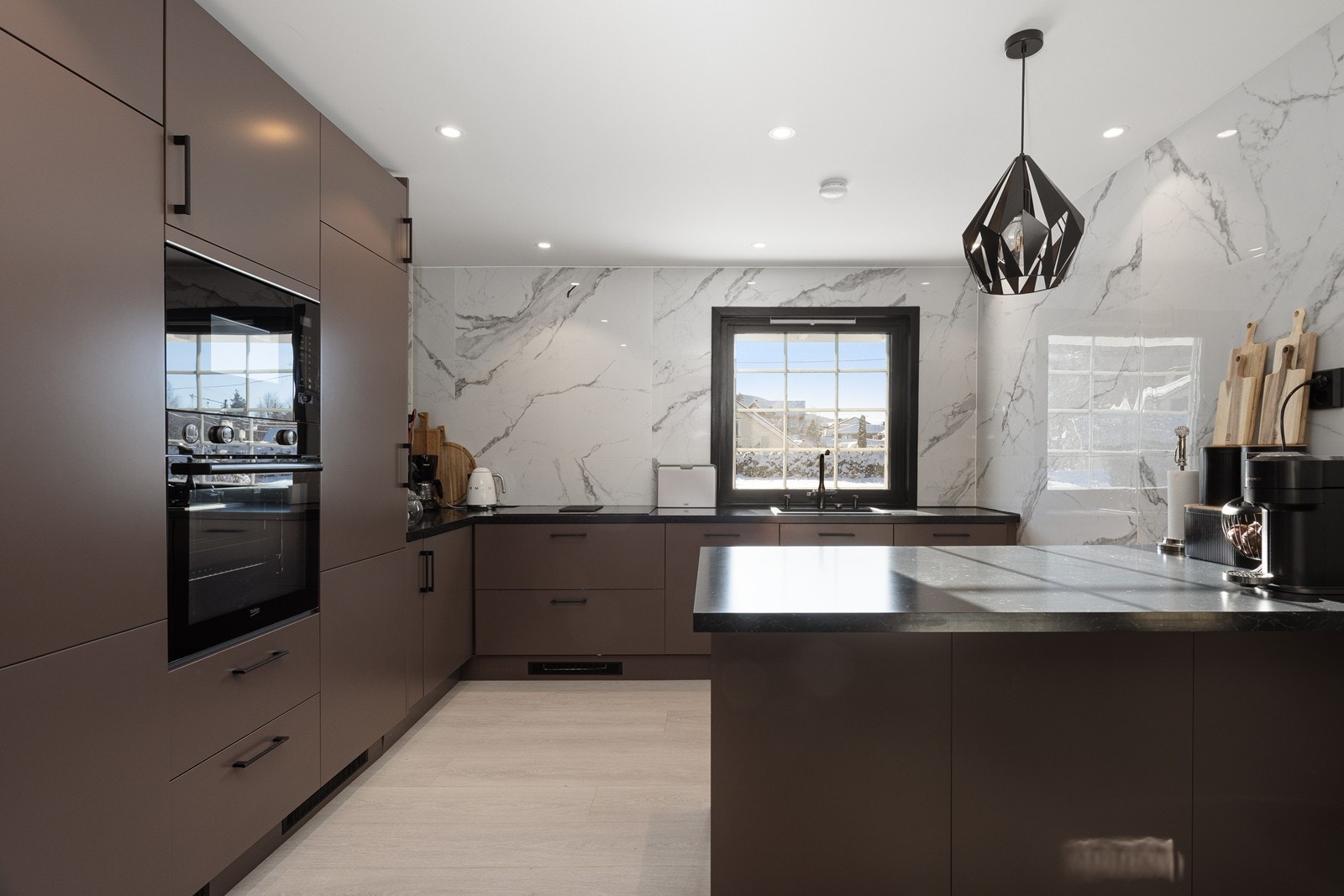 Delikat og moderne kjøkkeninnredning med trendy, glatte fronter og benkeplate av laminat. Kjøkkenet er utstyrt med integrerte hvitevarer som oppvaskmaskin, induksjonsplatetopp, stekeovn, micro kjøl/fryseskap Galleribilde