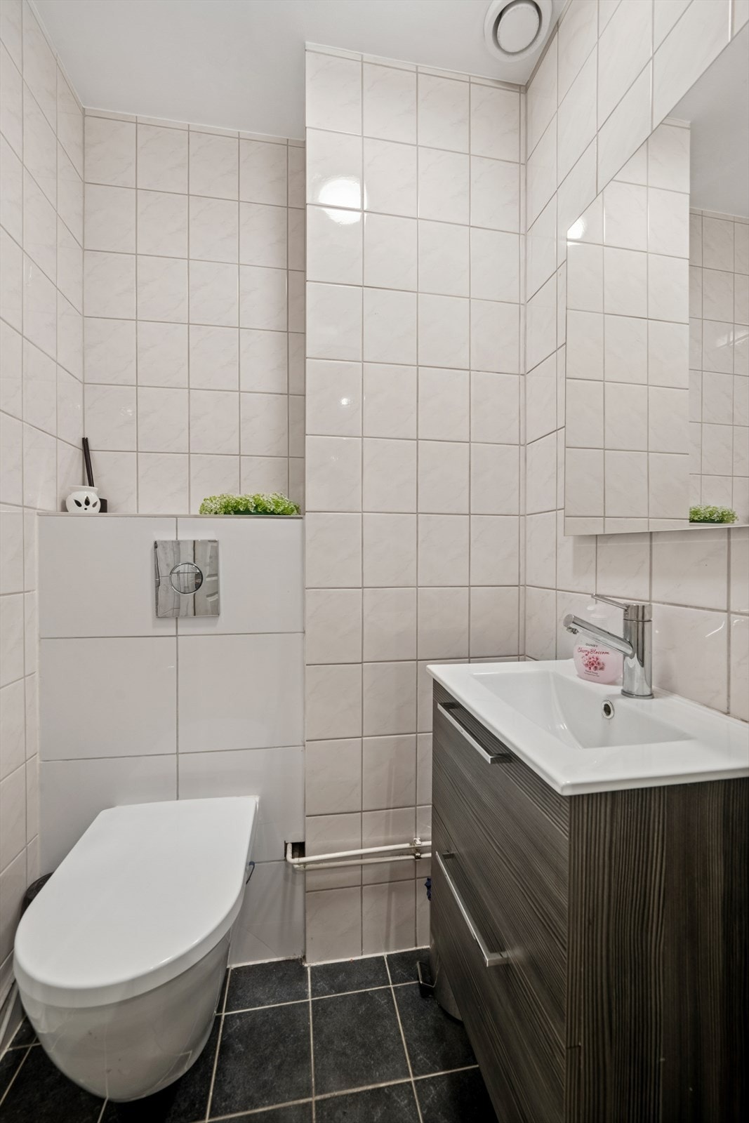 Separat toalettrom med fliser på gulv og vegger og malte flater i himling. Rommet er innredet med vegghengt toalett og servant med underskap. Det er mekanisk ventilasjon. Galleribilde