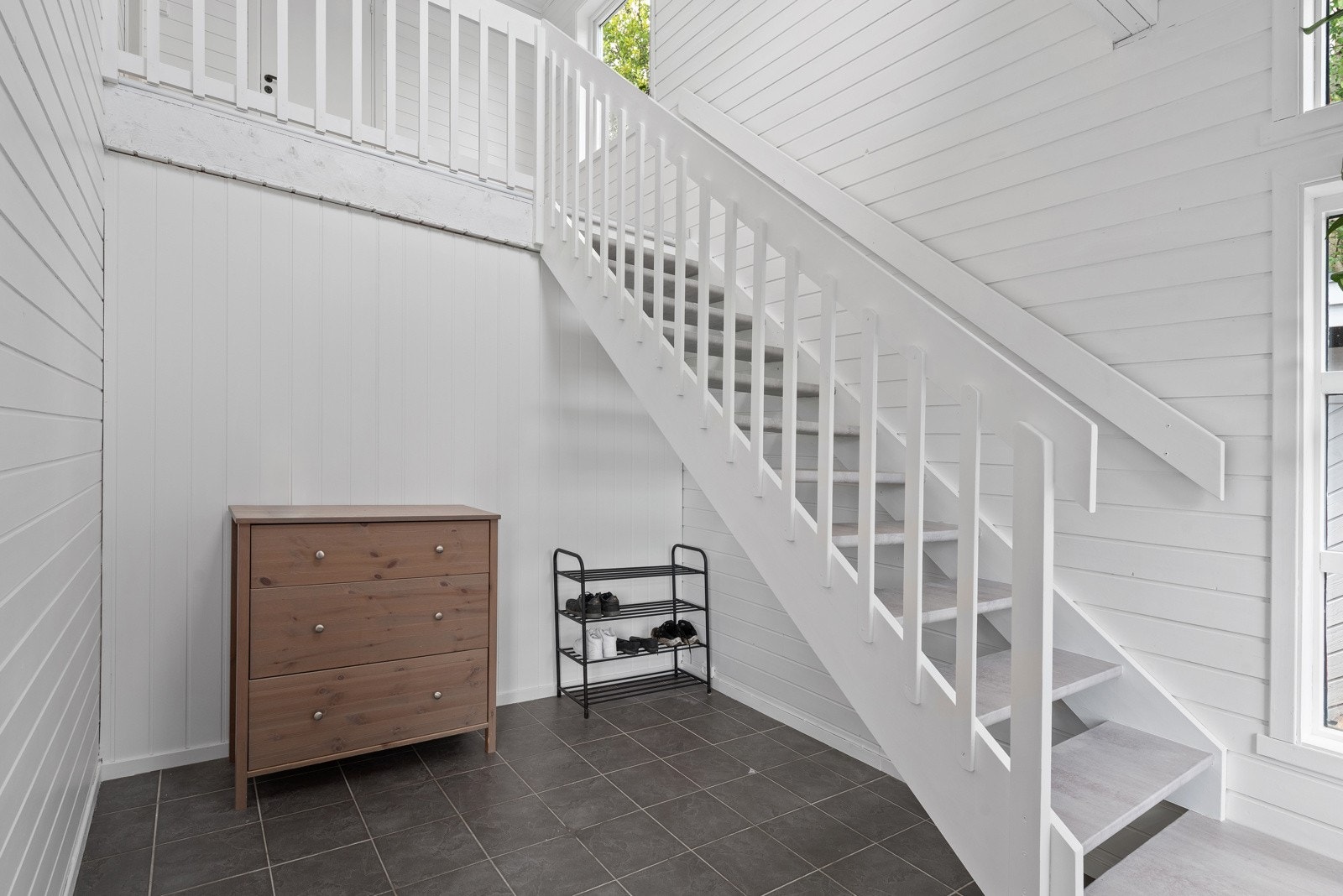 Romslig og luftig hall med gode plassmuligheter for større garderobeløsninger etter ønske og behov. Det er malt panel på veggene og grå fliser på gulv med behagelig gulvvarme. Galleribilde