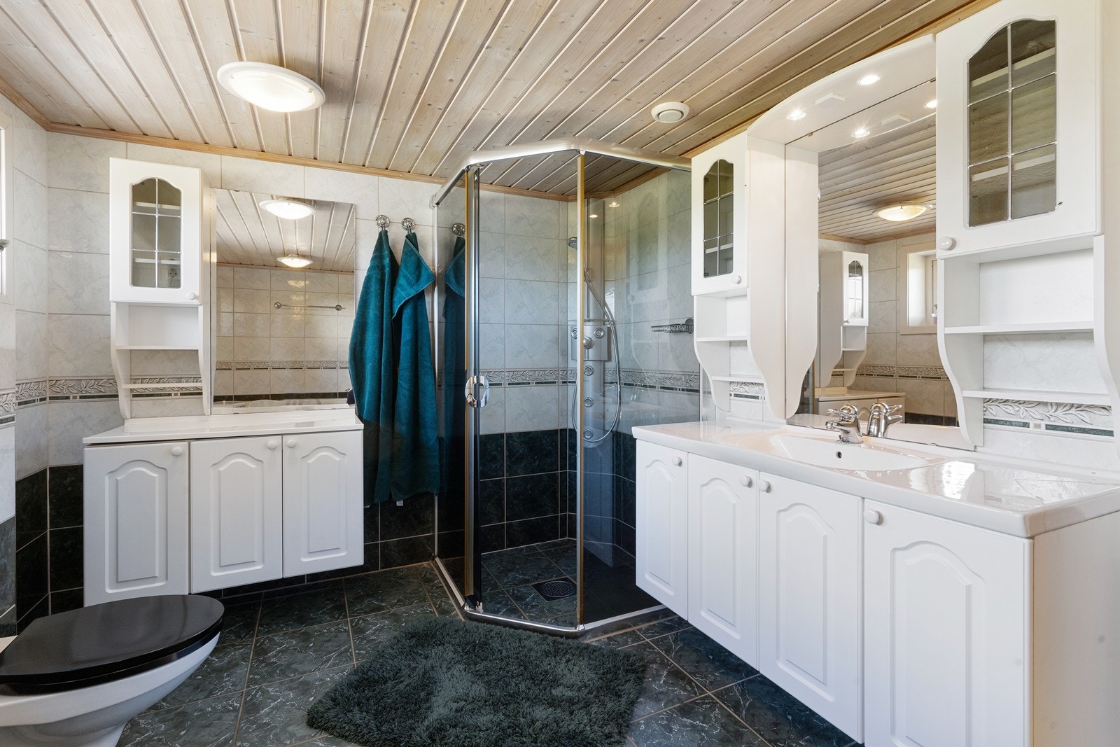 Flislagt bad med dusjhjørne, wc, og servant på hvit profilert innredning Galleribilde