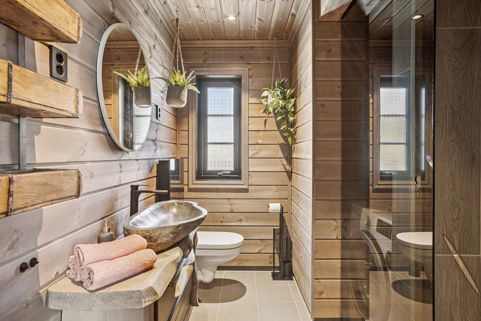 Delikat bad med flislagt gulv, trepanel, vegghengt toalett og en romslig dusjnisje med glassdør. Galleribilde