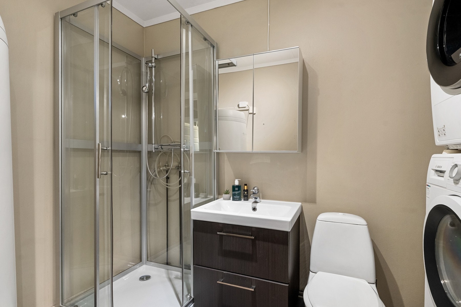 Bad/vaskerom - Flislagt gulv med elektriske varmekabler. Innredning med nedfelt servant, toalett, dusjkabinett og opplegg for vaskemaskin. Galleribilde