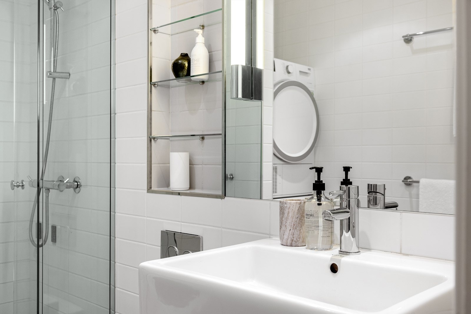 Badet er innredet med servant og underskap, speil med belysning, vegghengt toalett og dusjhjørne med svingbar dør i herdet glass. Galleribilde