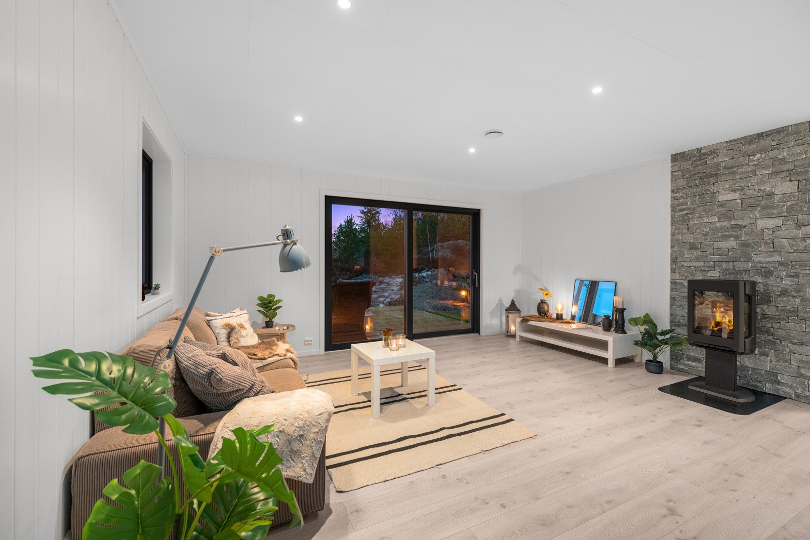 Pipeveggen er kledd med vakker naturstein og foran denne er det montert en moderne peisovn med stort glassfelt, slik at flammene kan sees fra hele rommet Galleribilde