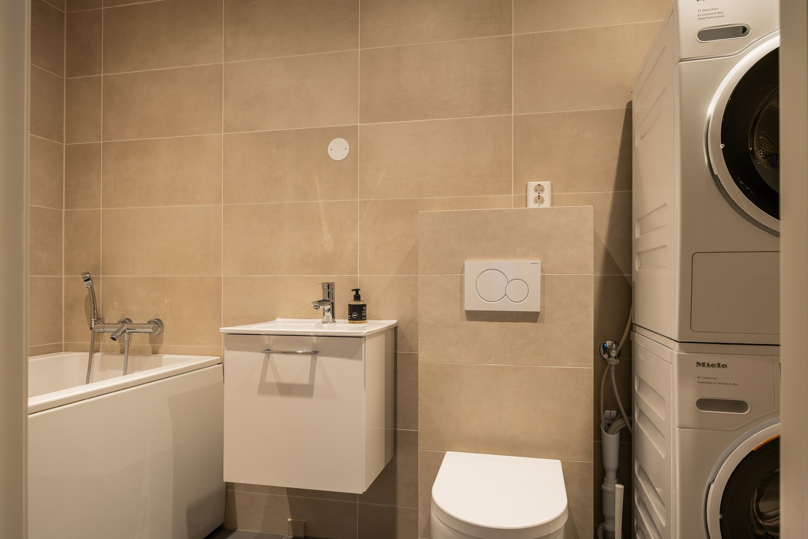 Flislagt bad i u.etg. med badekar, servant med ett greps blandebatteri og vegghengt toalett. Opplegg for vaskesøyle. Galleribilde