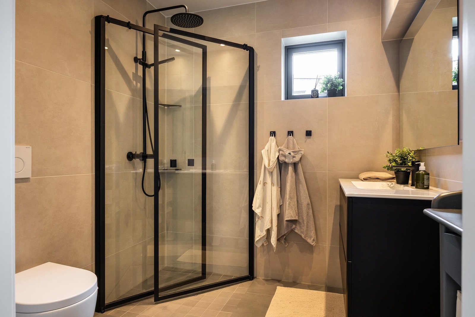 Flislagt bad med nedsenket dusjnisje og innfellbare dusjdører og vegghengt toalett. Galleribilde