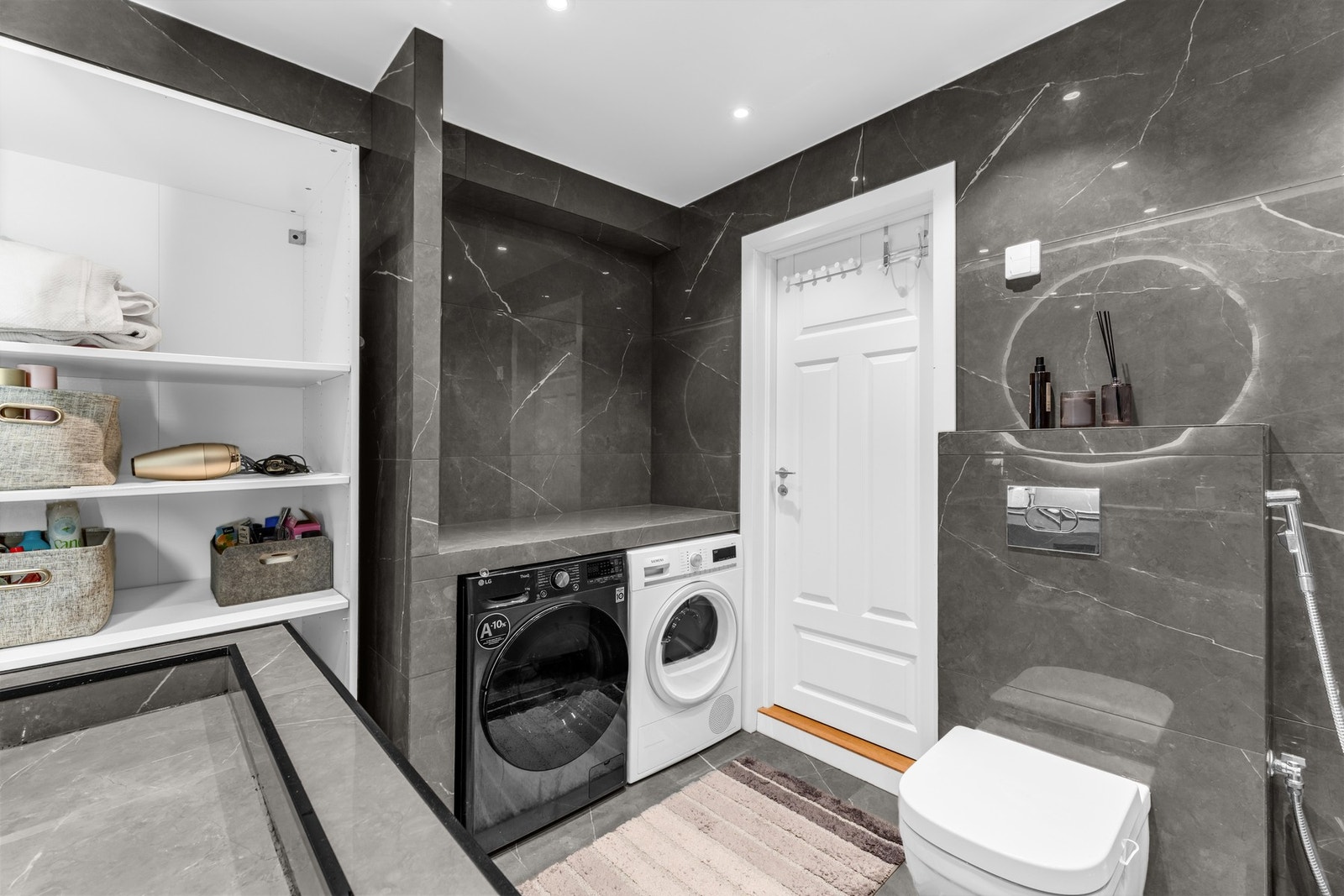 Badet har opplegg for vaskemaskin og tørketrommel, samt praktiske oppbevaringshyller. Galleribilde