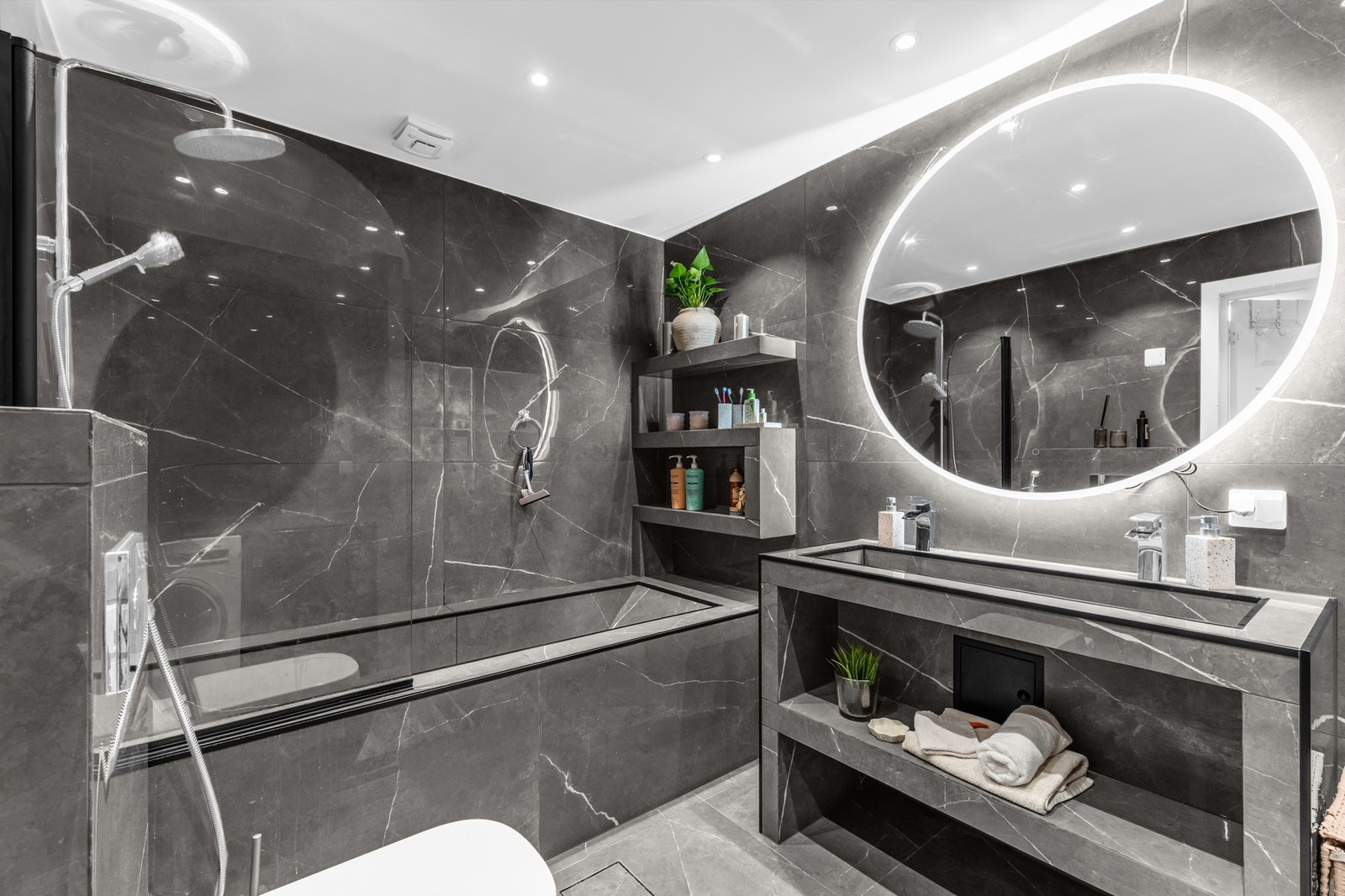Flislagt bad med varmekabler, innfliset badekar med dusj, servantseksjon og speil med integrert lys. Galleribilde