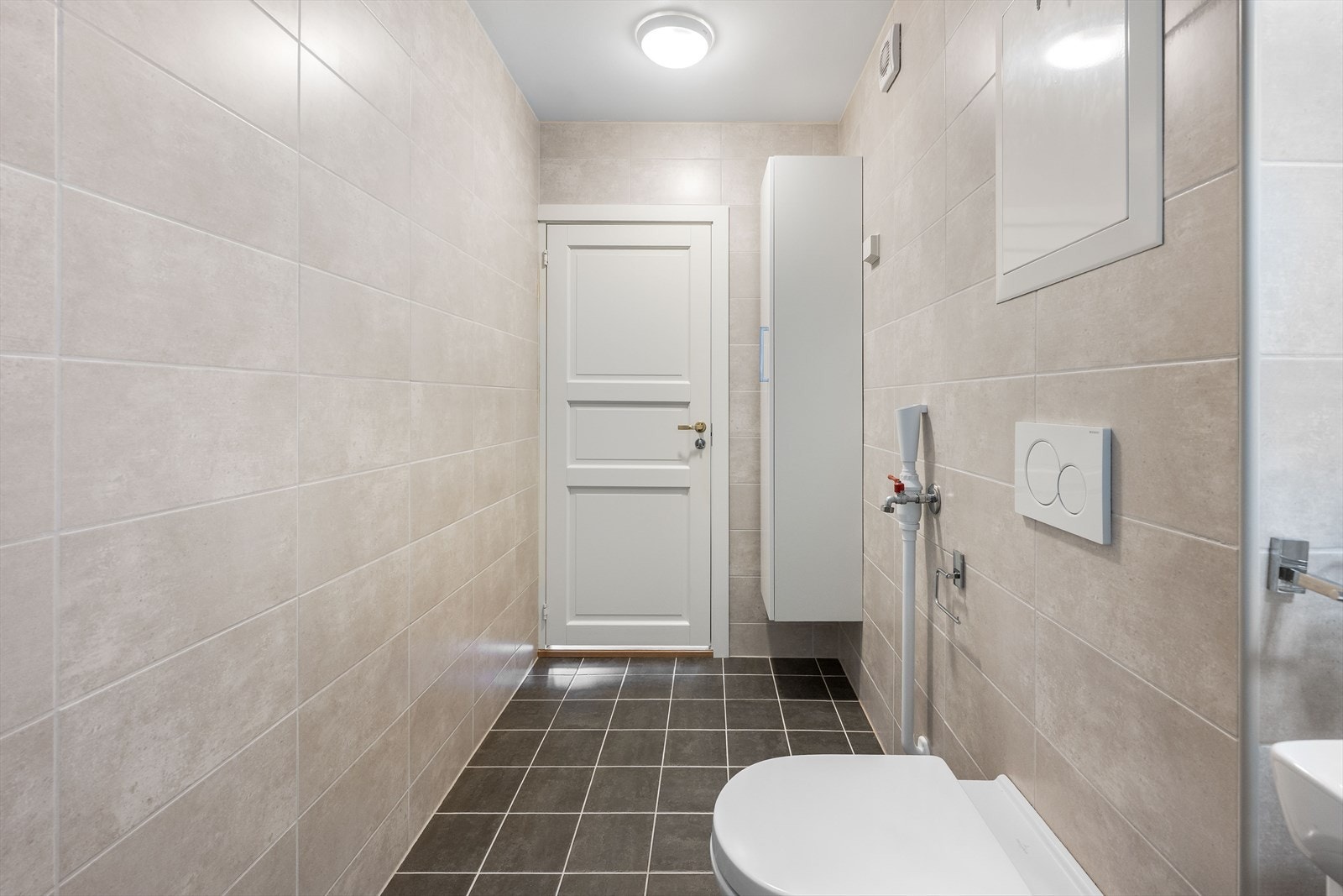 Badet har flislagte vegger, malte flater i tak og flislagt gulv med gulvvarme. Badet er innredet med veggmontert WC, dusjplass med inn-utadslående dusjvegger, servant med ettgreps blandebatteri i innredning og opplegg for vaskemaskin. Galleribilde