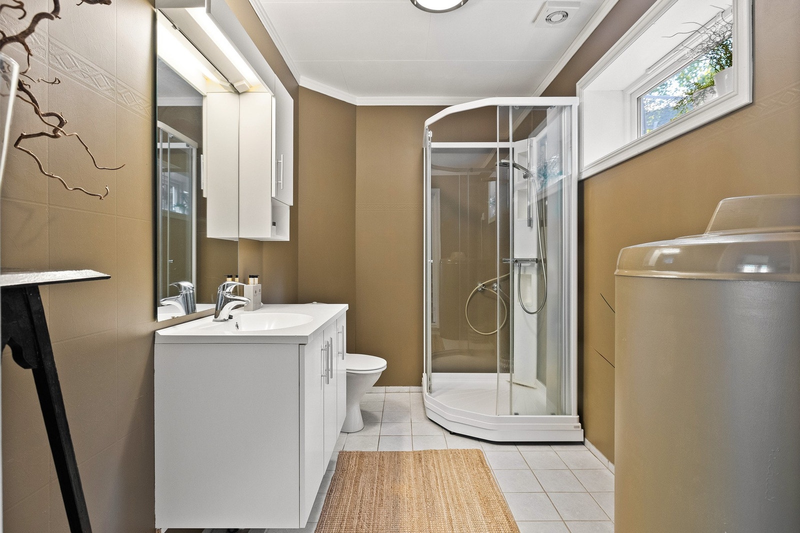 Baderommet er utstyrt med vegghengt servantskap med dører og overskap og heldekkende servant med ett-greps armatur. Badet har gulvmontert toalett og dusjkabinett med glassdører. Galleribilde