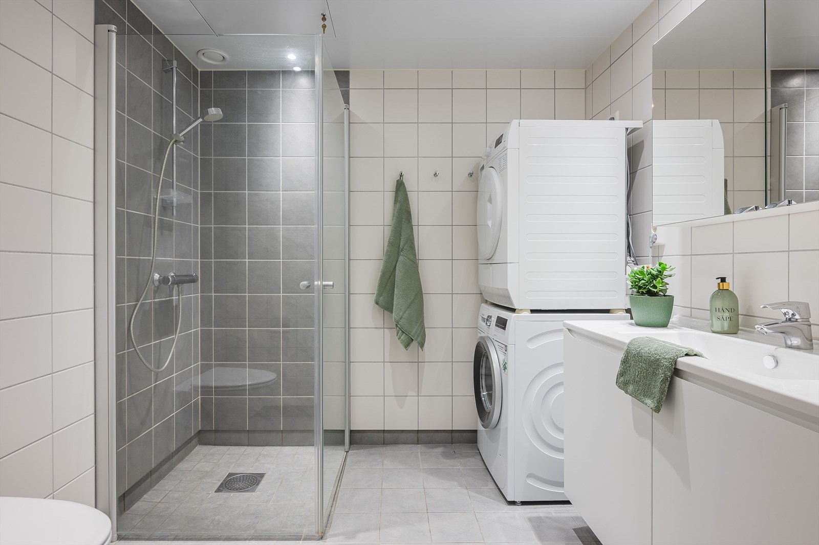 Lekkert, stilrent bad fra 2018 innredet med servant på innredning, toalett og dusjhjørne med glassvegger. Opplegg for vaskemaskin og tørketrommel. Galleribilde