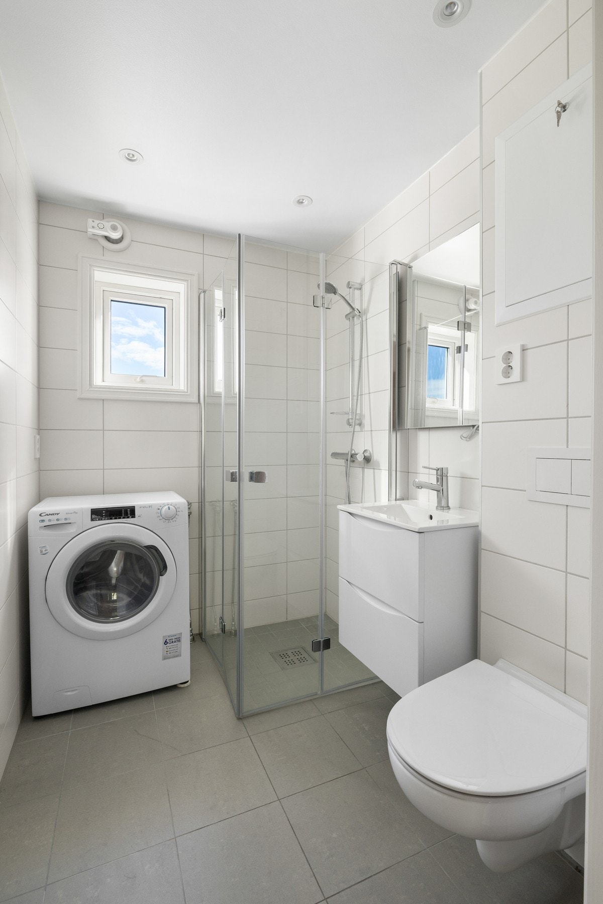 Store fliser i ulike gråtoner bidrar til et stilrent uttrykk. Opplegg for vaskemaskin er etablert, og badet har varmekabler, vegghengt toalett og et nedsenket dusjhjørne med innfellbare dører. Galleribilde