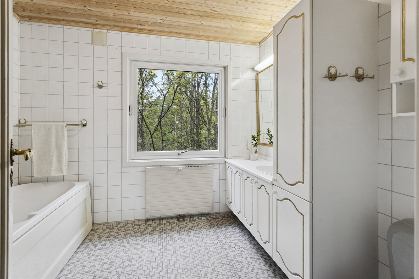 Baderommet i første etasje har mosaikkfliser på gulvet, panel i himlingen og et deilig badekar. Badet er fra byggeår og har behov for modernisering. Galleribilde