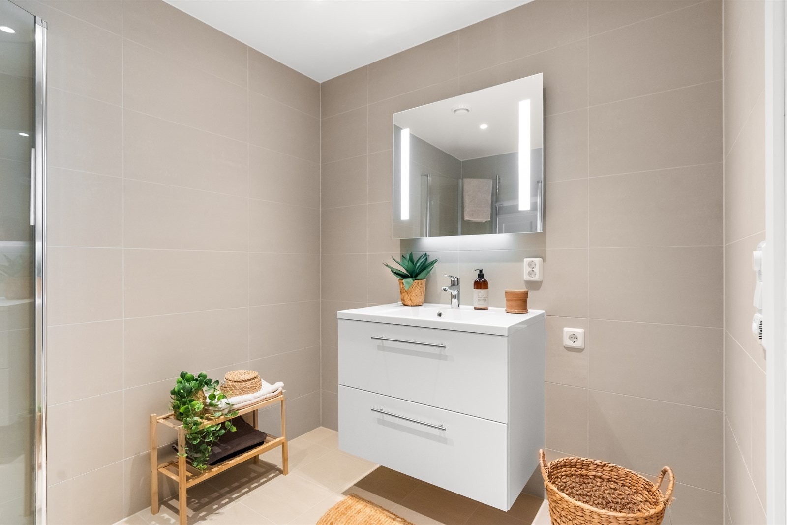 Det er baderomsmøbel og vegghengt speil, vegghengt toalett, dusjhjørne og opplegg for vaskemaskin og tørketrommel. Galleribilde