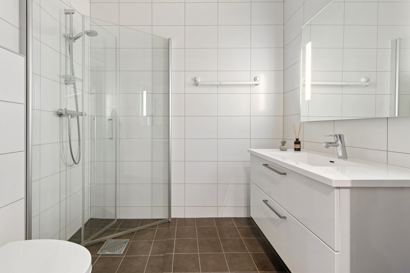 Rommet er innredet med en åpen dusjløsning, vegghengt toalett og servantinnredning. Galleribilde