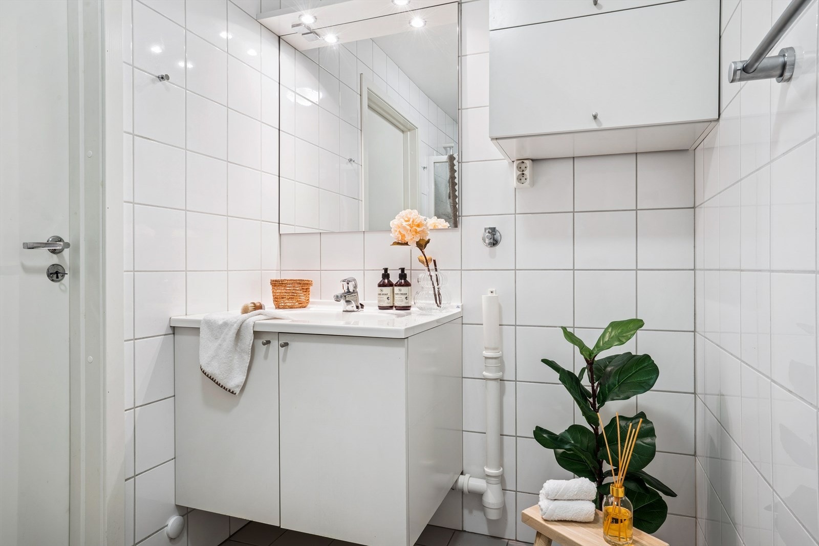 Pent, flislagt bad utstyrt med gulvmontert toalett, innredning med servant og dusjvegger av glass med dusjgarnityr på vegg. Galleribilde