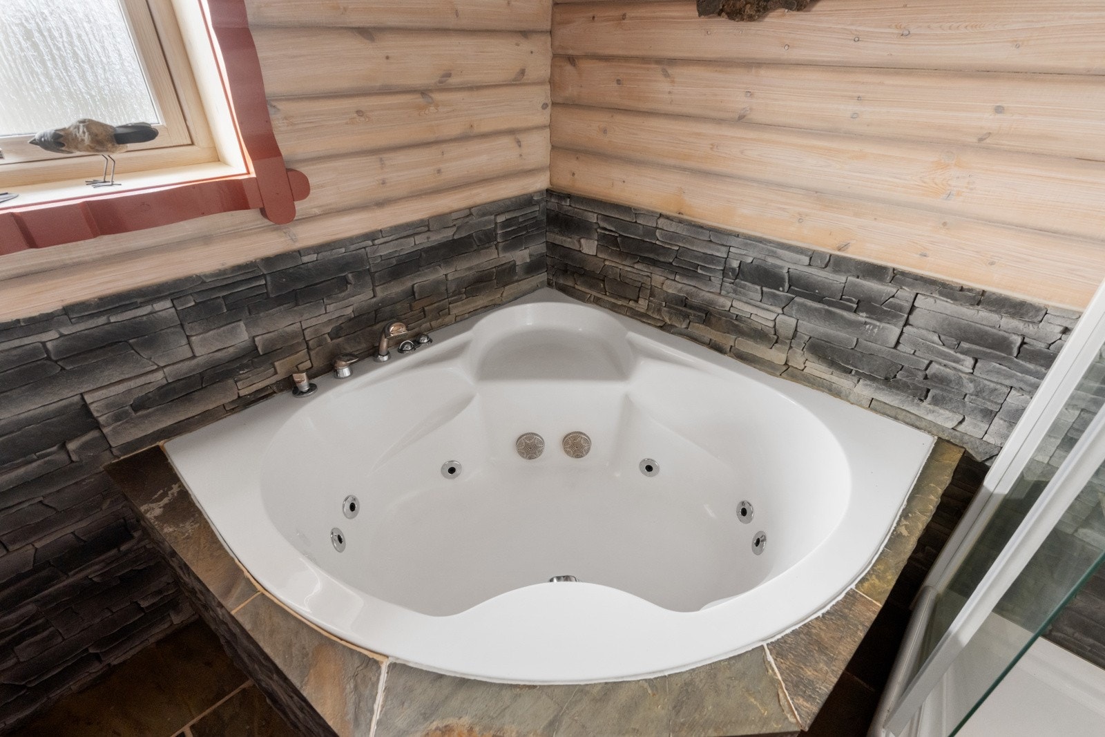 Badet er utstyrt med dusjkabinett, et boblekar kledd med fasadestein, samt en servant med skap Galleribilde