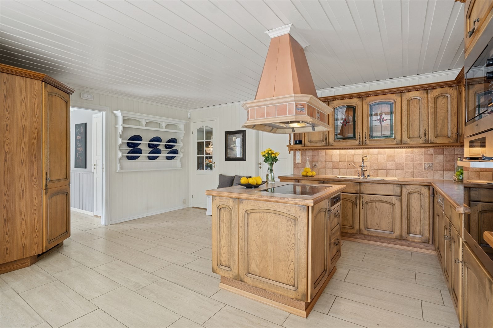 Det er nedfelt kum i rustfritt stål, og det er fliser på veggen over benker og belysning under overskapene. Medfølgende stekeovn, induksjonstopp, oppvaskmaskin og kjølehjørne er integrert i innredningen. Galleribilde