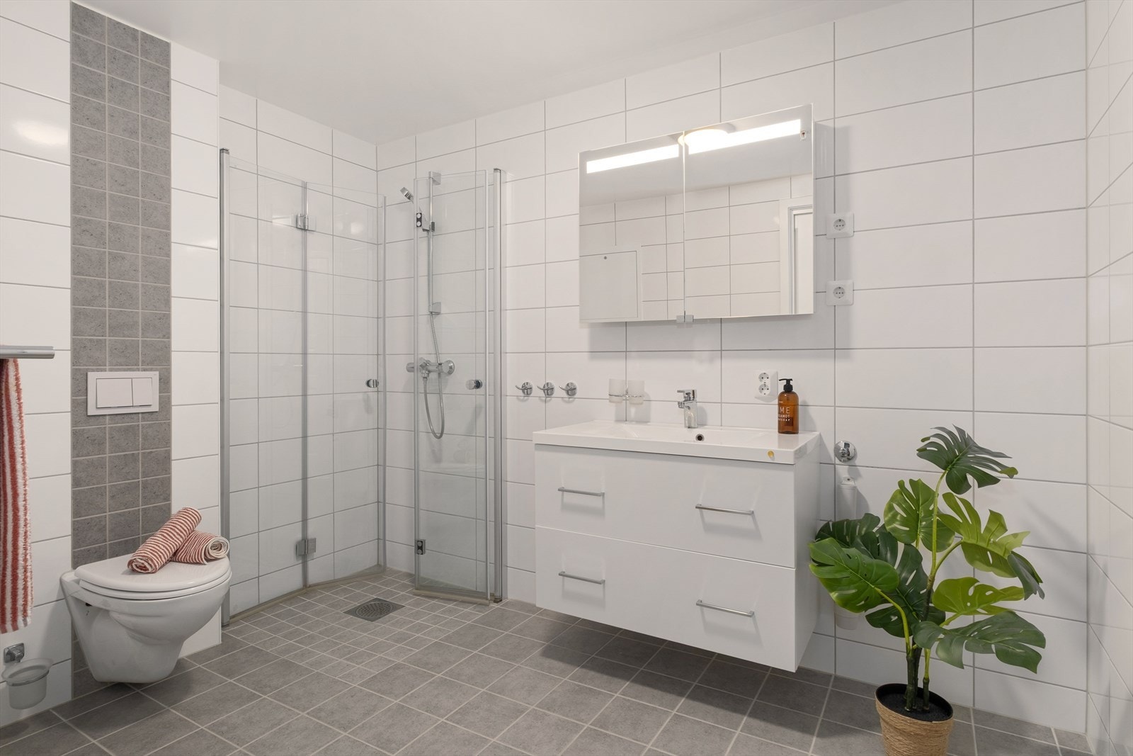 Badet er innredet med baderomsinnredning med servant, vegghengt toalett, dusj og opplegg for vaskemaskin. Galleribilde