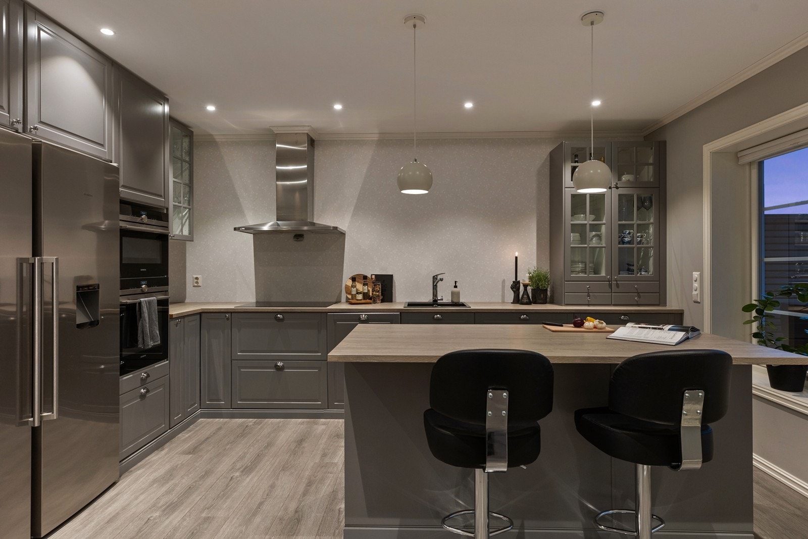 Stilig kjøkkenløsning med integrert stekeovn, platetopp, mikrobølgeovn og oppvaskmaskin samt koselig øy med spiseplasser Galleribilde