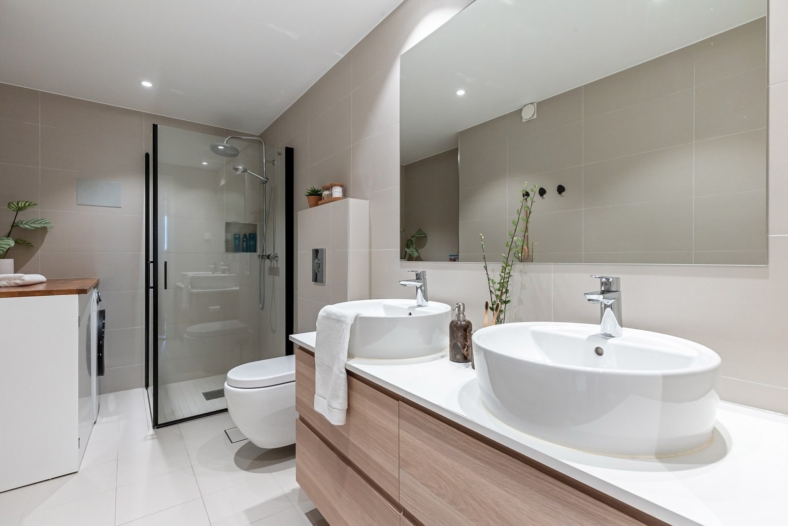 Badet er lyst og delikat innredet. Her er det to servanter på skuffeinnredning, vegghengt toalett, dusj med innfellbare dusjfører og opplegg for vaskemaskin. Galleribilde