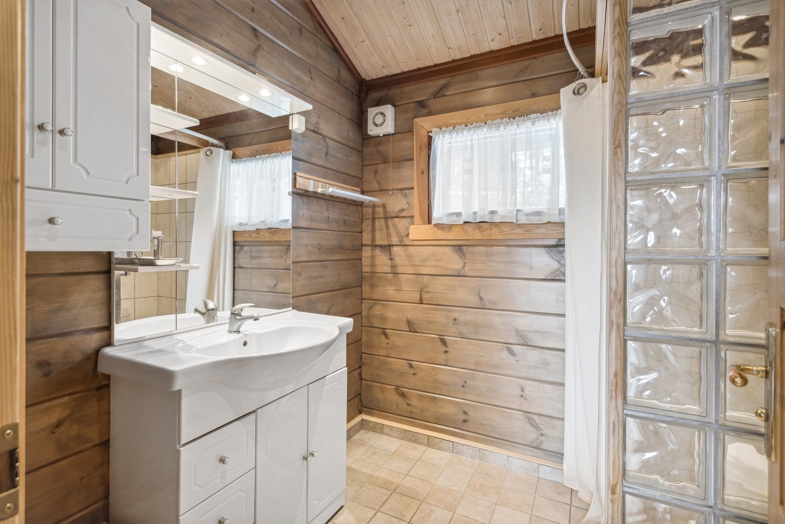 Pent bad innredet med servant på innredning, dusjhjørne og toalett. Galleribilde