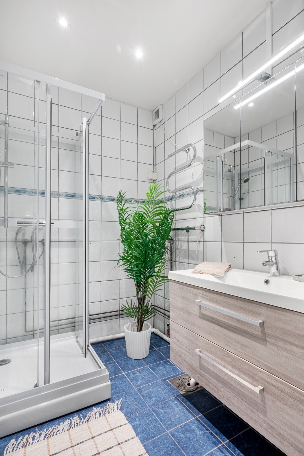Badet har flislagte overflater, gulvvarme og downlights. Innredningen består av dusjkabinett, servant, speilskap med lys og opplegg for vaskemaskin. Galleribilde