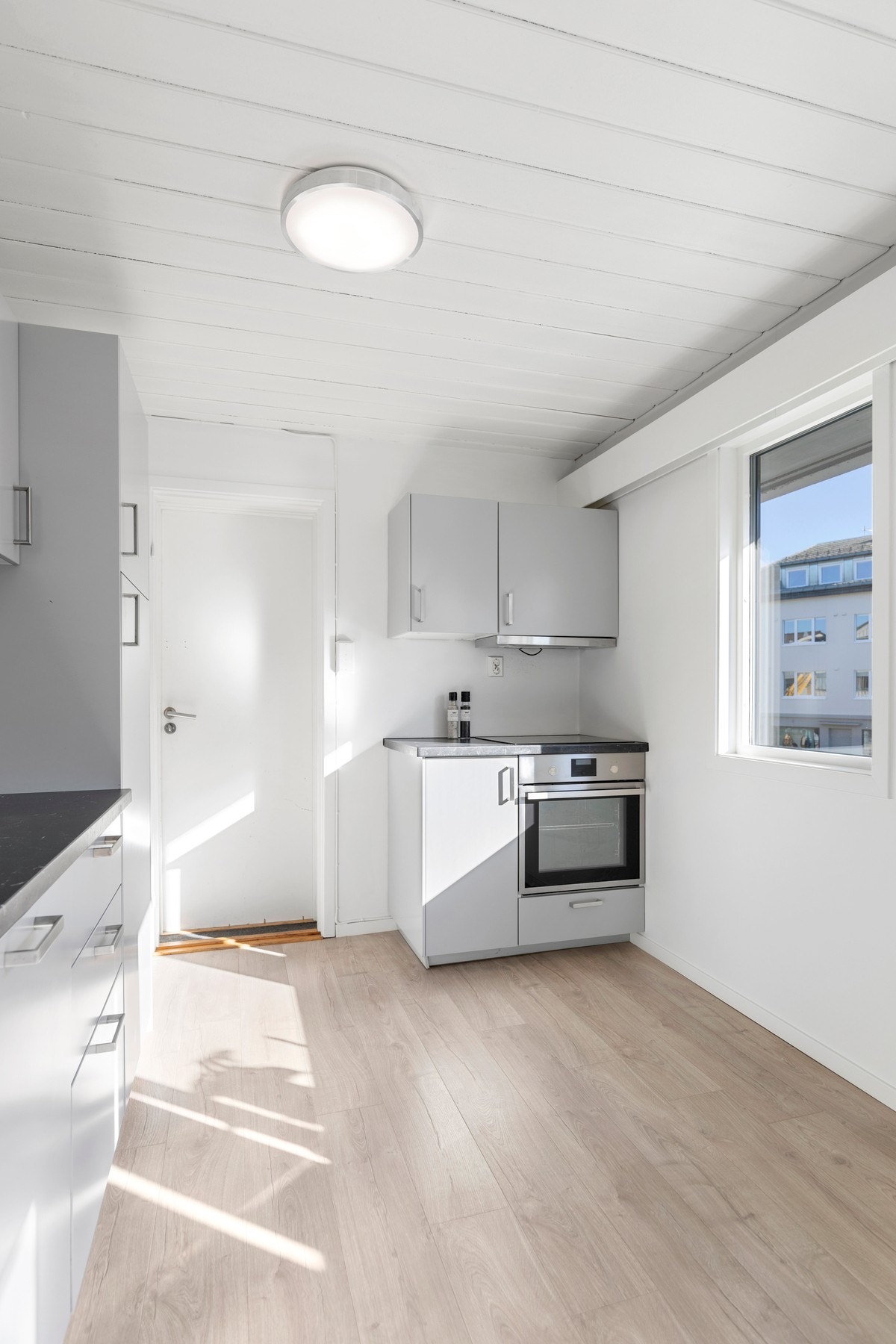 Kjøkkeninnredning i grå, slette fronter, laminat benkeplate, ventilator og integrerte hvitevarer; stekeovn, platetopp og oppvaskmaskin. Galleribilde