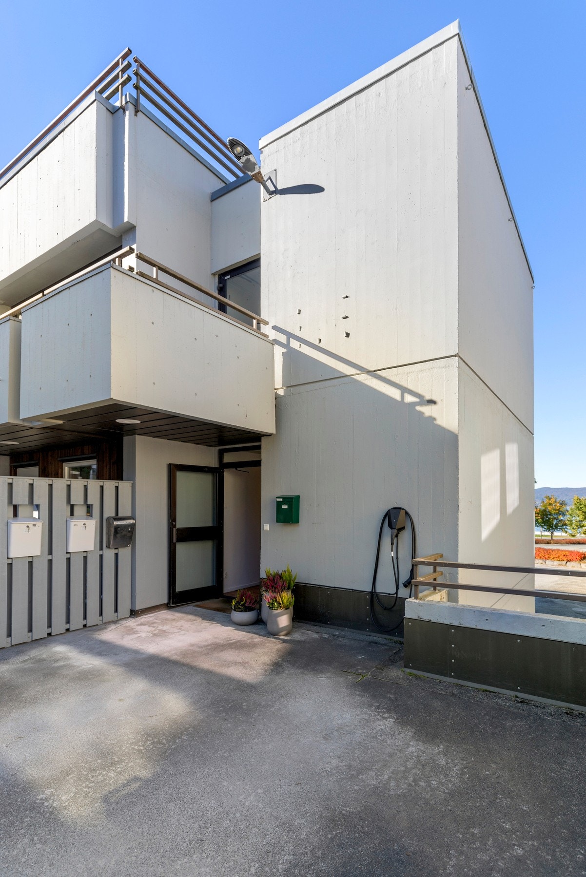 Biloppstillingsplass på fellesareal, like utenfor inngangsdøren. Ved inngangspartiet er det montert Easee elbil-lader. Galleribilde