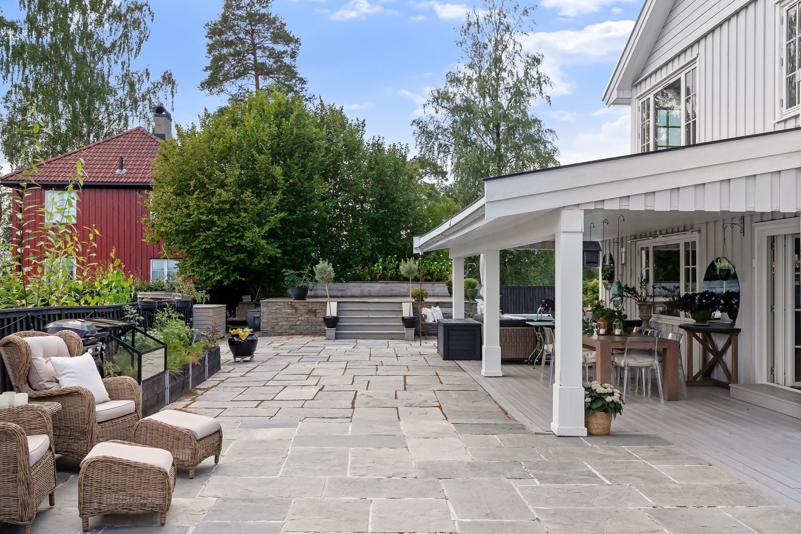 Stor, skiferbelagt terrasse over to nivåer, som strekker seg langs hele sydøstsiden av bygget og over i hagen.