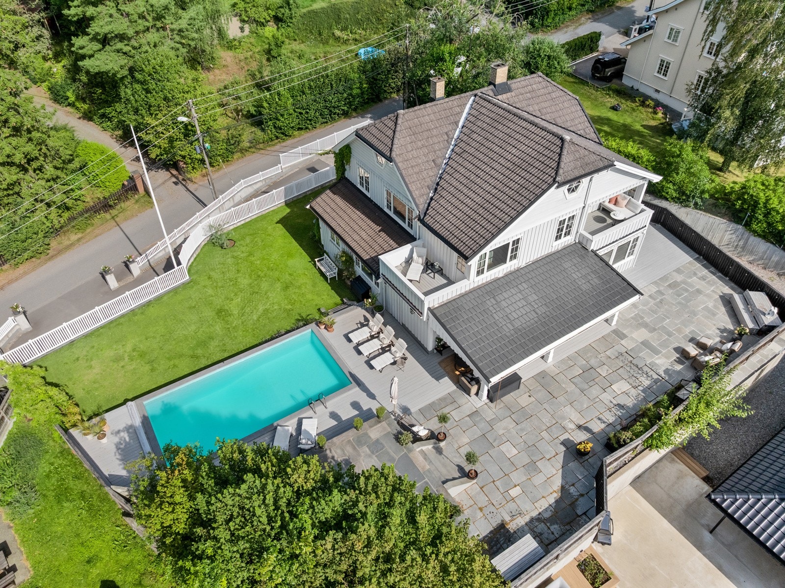 Hagen rammes inn av hvitmalte gjerder og lubne prydbusker, og har en høy plassering over garasjeanlegget, noe som hindrer innsyn fra veien og gjør det hele privat.