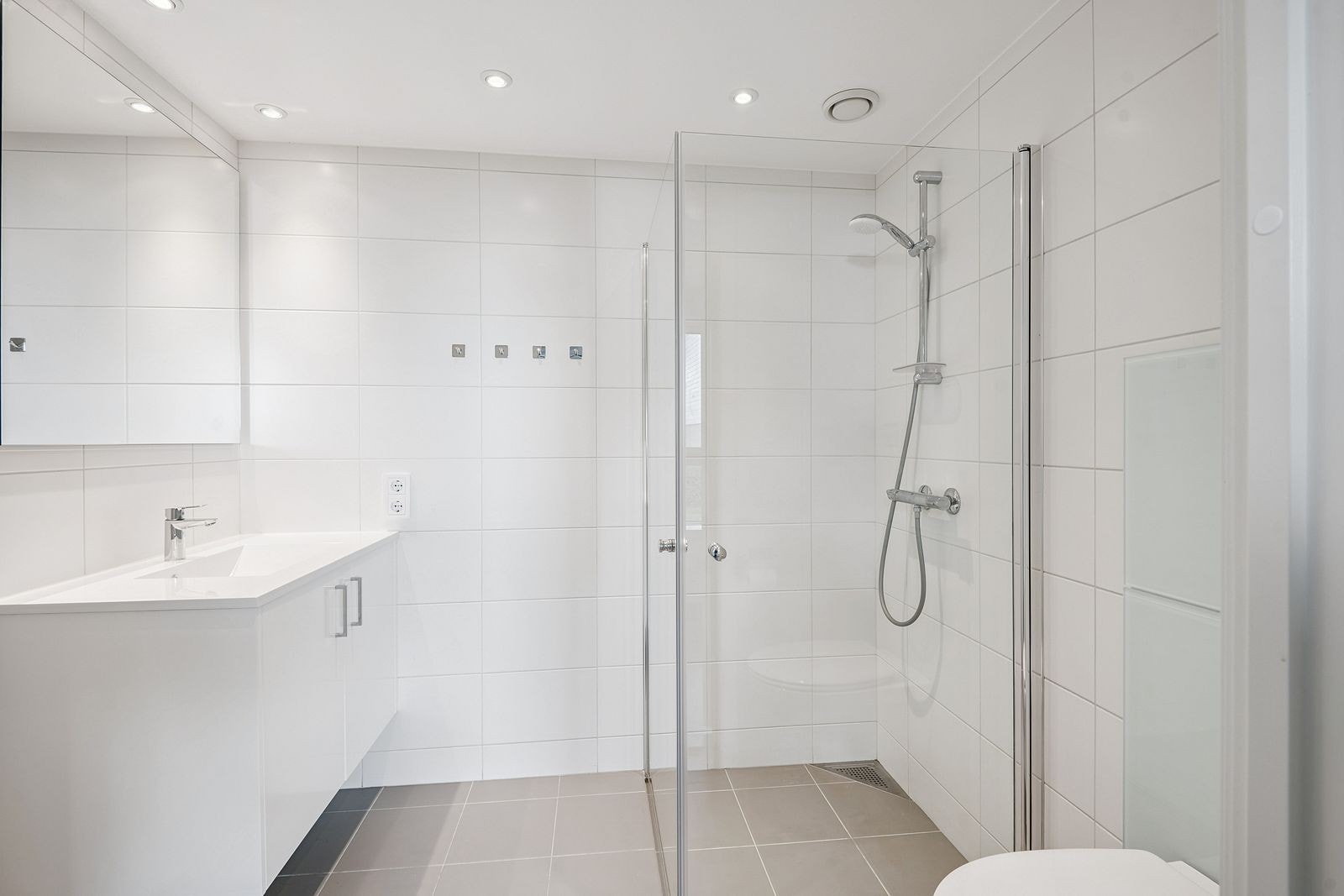 Lekkert flislagt bad med dusjhjørne, gulvvarme og opplegg for vaskemaskin. Galleribilde