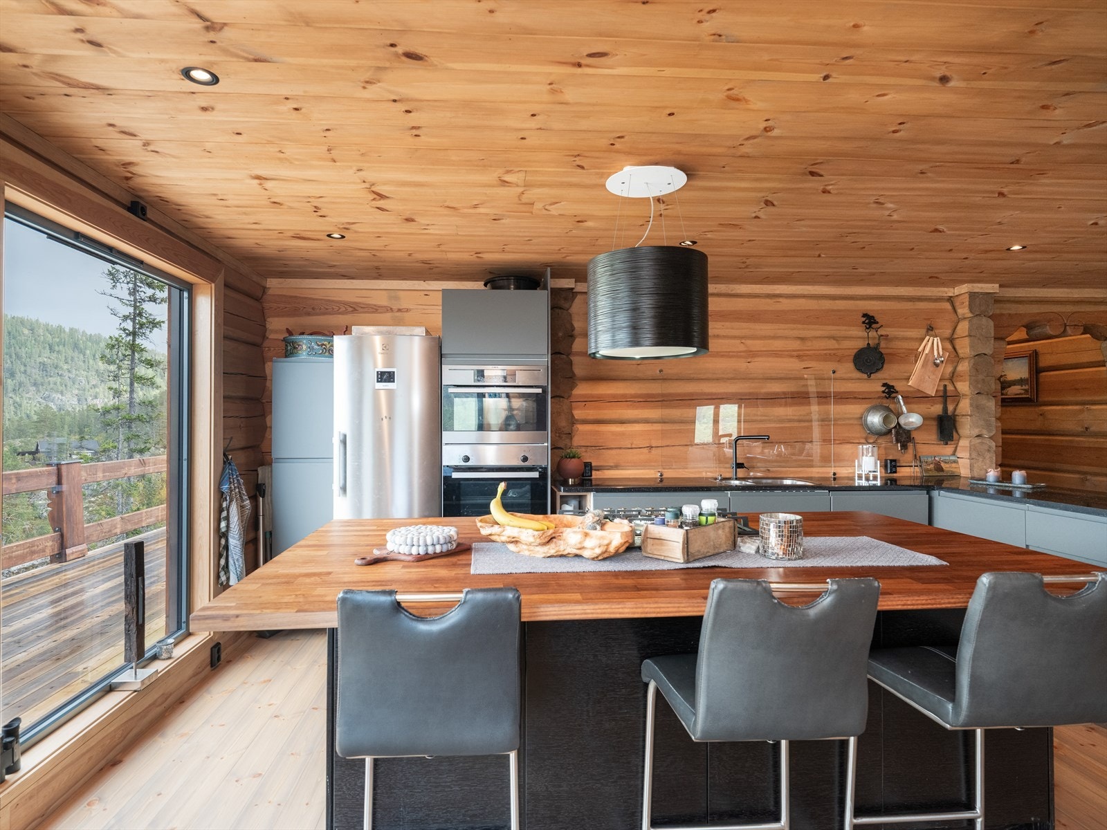 Stor kjøkkenøy med tre frokostplasser på den ene siden, hvor vinduene slipper rikelig med naturlig lys inn til spiseplassen. Galleribilde