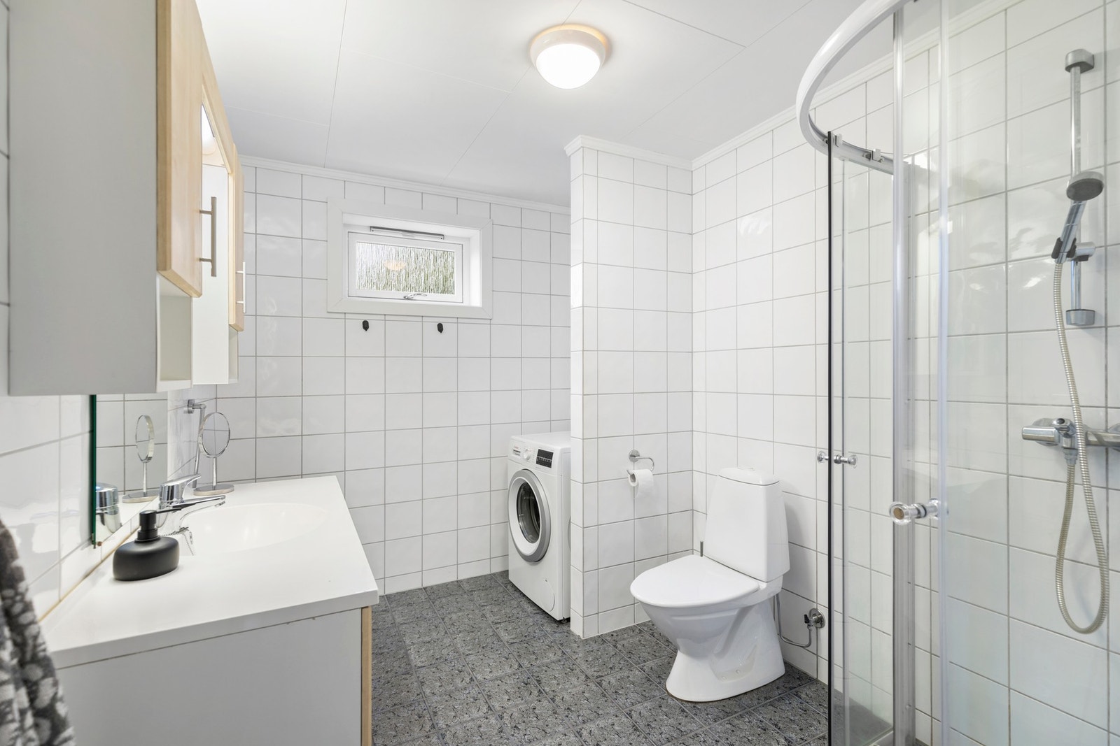 Badet/vaskerommet i denne etasjen ble også renovert i 2006, og har helfliset utførelse. Av utstyr er det montert gulvvarme, vaskemaskin, wc, dusjnisje med glassdør, baderomsinnredning med helstøpt servantplate og avtrekksvifte. Nye vann og avløpsrør også Galleribilde