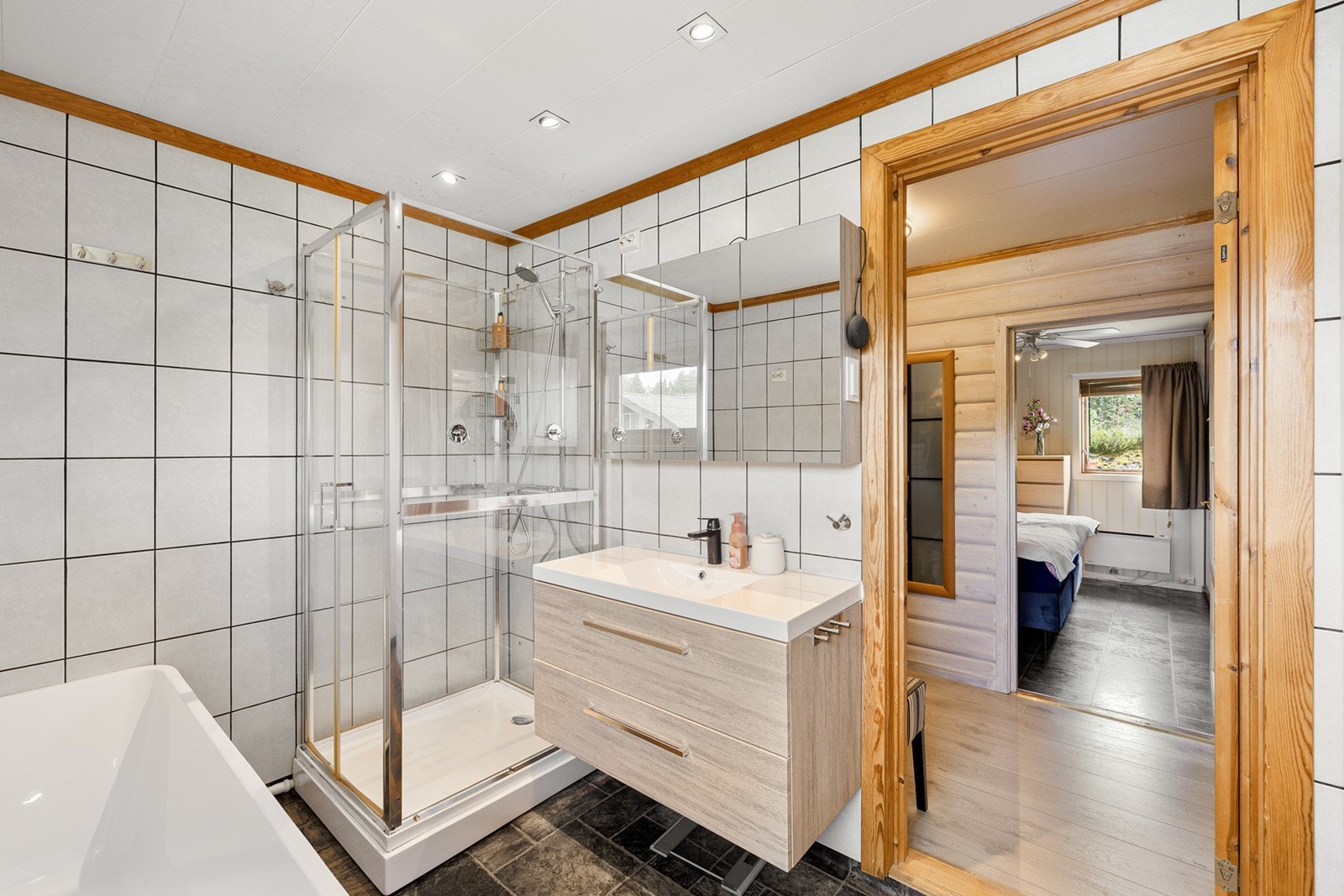 Badet er innredet med dusjkabinett og et stort frittstående badekar. Fliser på gulv og vegg med varmekabler i gulv. Galleribilde