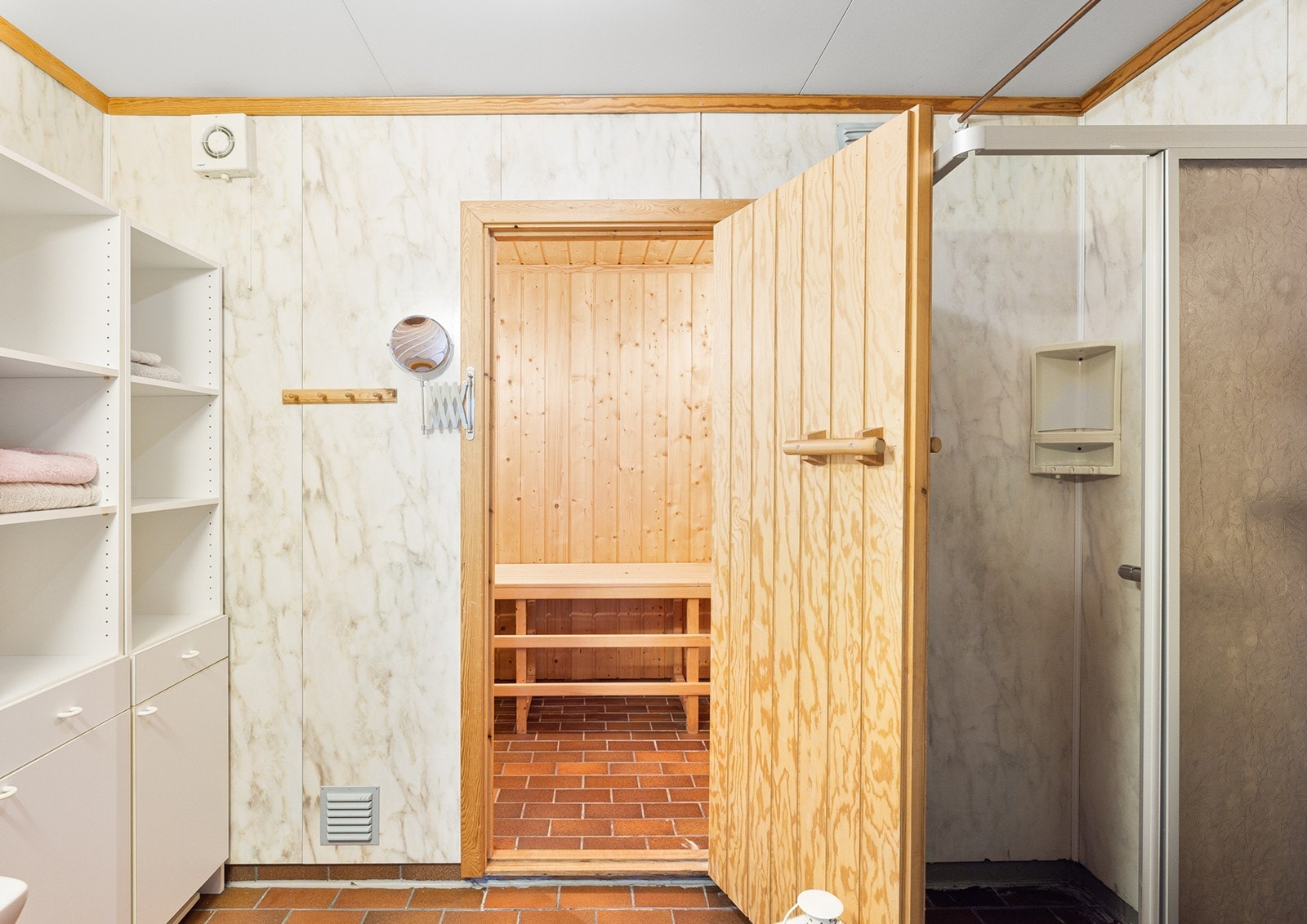 Badet har flislagt gulv og vegger med lys baderomspanel. Innredet med toalett, dusjsone og servant med speil. Galleribilde